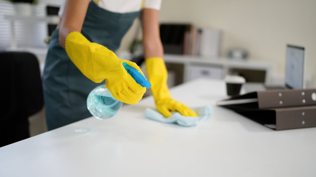 Profesional de limpieza con guantes y delantal desinfectando una superficie de trabajo