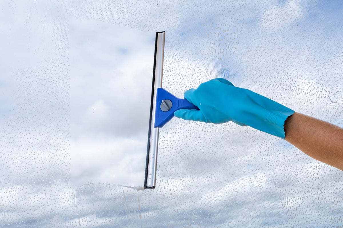Persona con guante azul limpiando un cristal con una bayeta y agua jabonosa