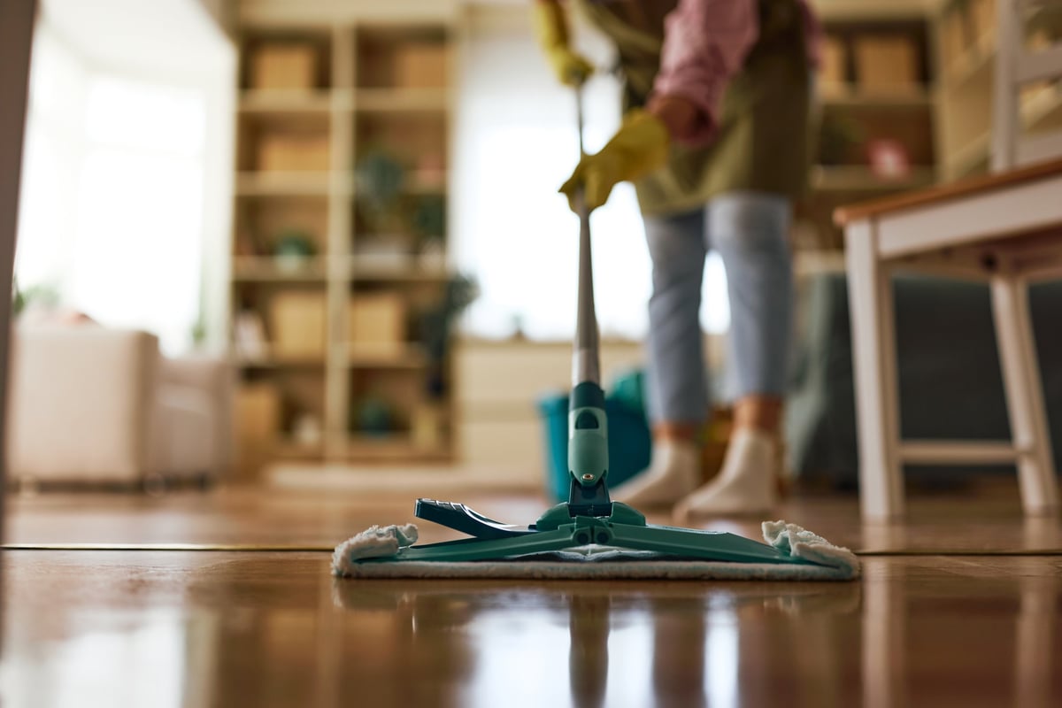 Persona con guantes y delantal limpiando a fondo el suelo de una vivienda con una mopa plana